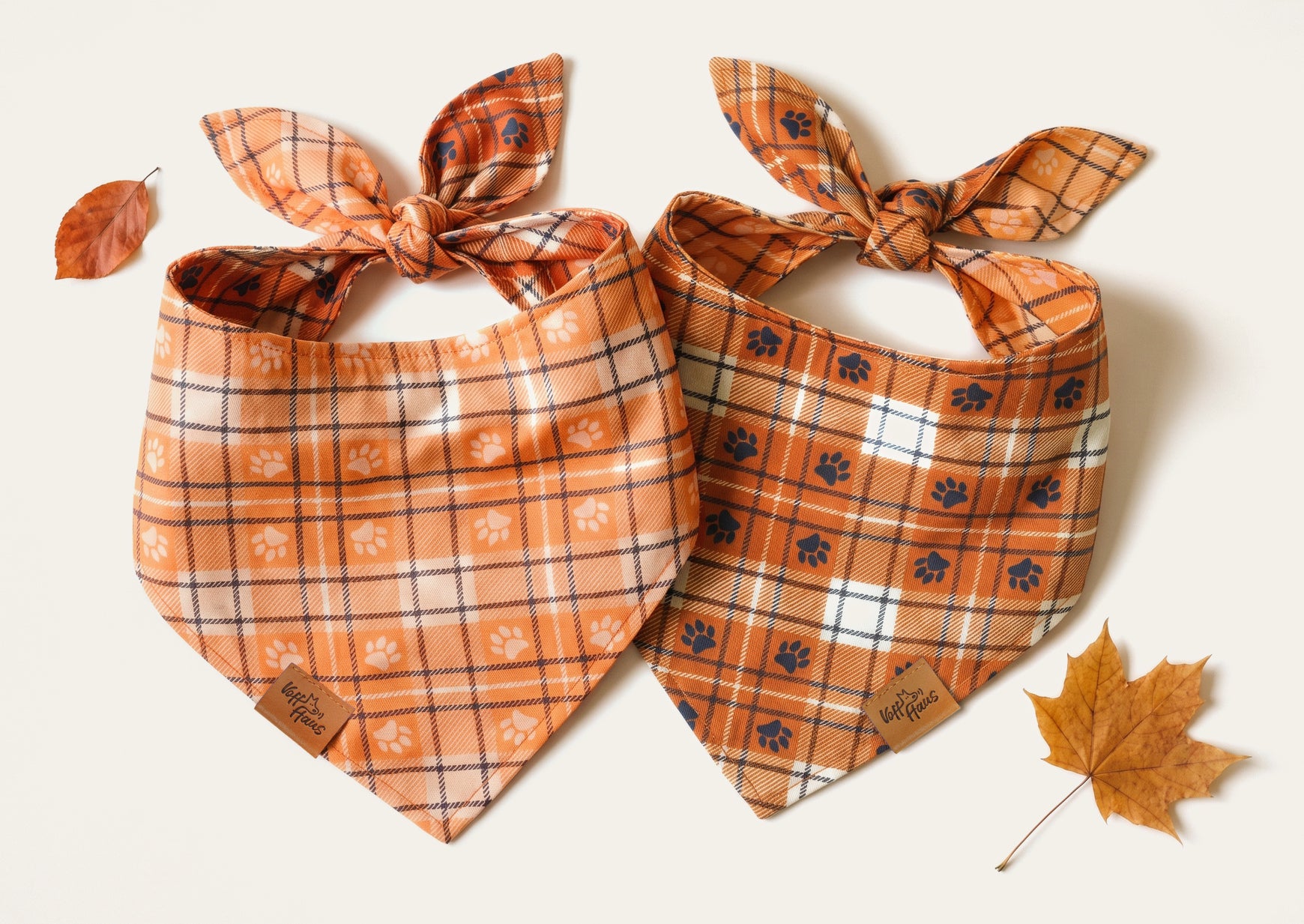Both sides of the Plaid Paws reversible bandana, laid flat with autumn leaves